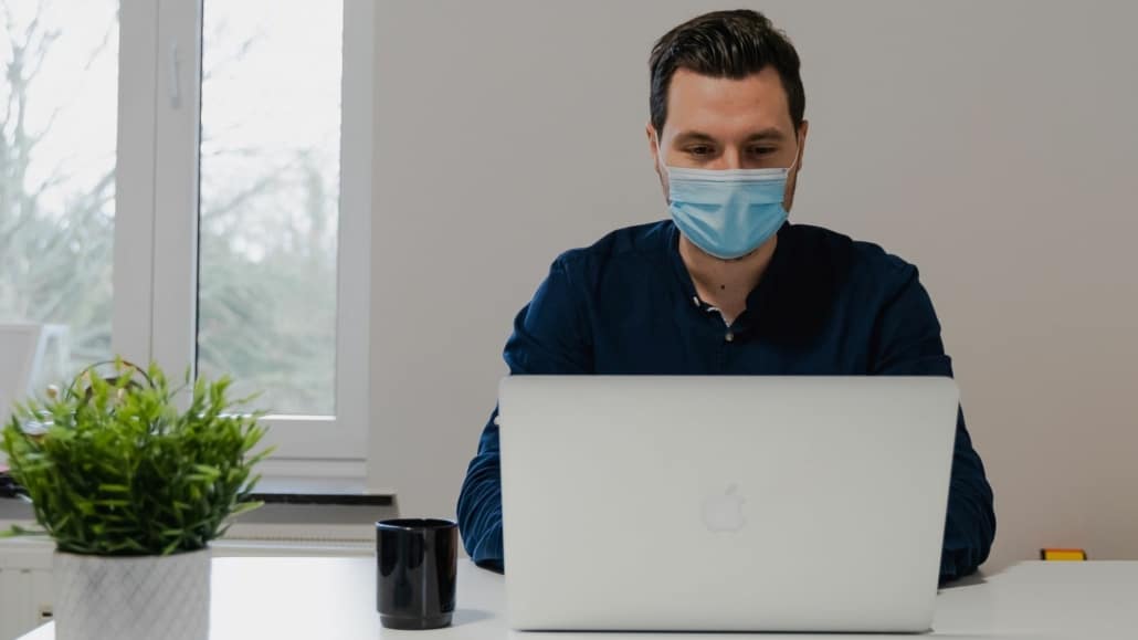 Man met mondkapje achter laptop