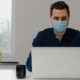 Man met mondkapje achter laptop